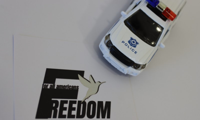 White toy police car resting near a "FREEDOM for all americans" graphic featuring a small bird silhouette