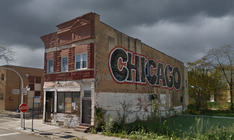 Weathered brick building with a large "CHICAGO" mural under a dark, rainy sky