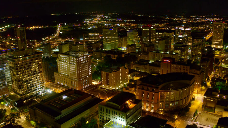 Nighttime aerial view of a cityscape in Virginia, featuring illuminated buildings, streets, and highways, highlighting the urban environment under the glow of city lights