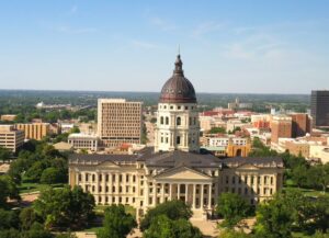 Aerial view of downtown Kansas City, featuring the prominent dome of the Kansas State Capitol building surrounded by other buildings, greenery, and clear blue skies, illustrating the context for discussing Kansas City's Crime Rate statistics.