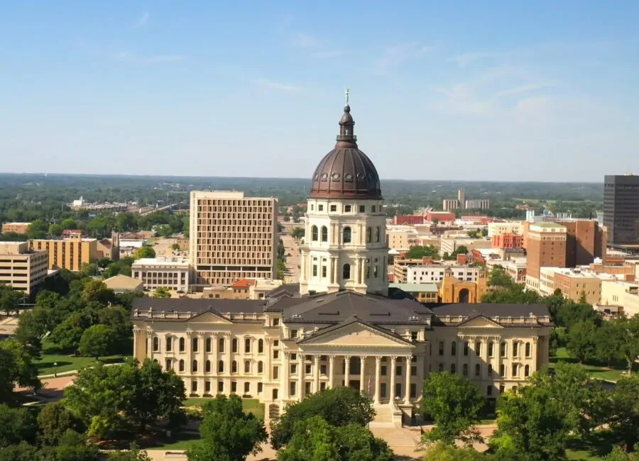 Aerial view of downtown Kansas City, featuring the prominent dome of the Kansas State Capitol building surrounded by other buildings, greenery, and clear blue skies, illustrating the context for discussing Kansas City's Crime Rate statistics.