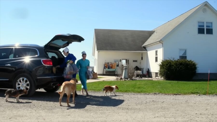 Mennonite Women in Traditional Attire Unload Groceries from An Suv Outside a Farmhouse, Reflecting Their Selective Use of Technology