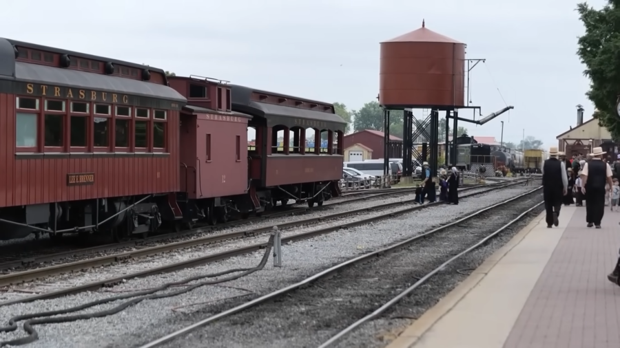 Amish Individuals, Dressed in Traditional Plain Clothing, Walk Alongside a Historic Train at A Railway Station, Highlighting the Community's Selective Integration with Modern Society While Maintaining Their Distinct Cultural Practices