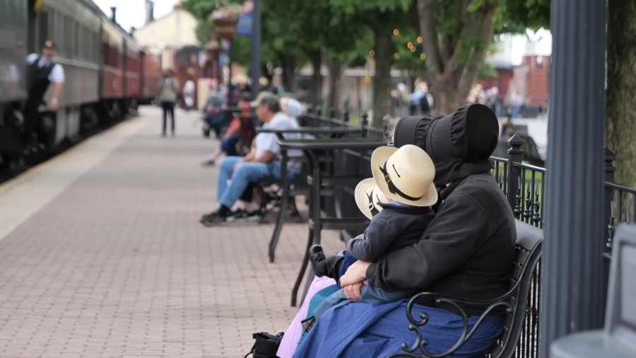 A Mennonite or Amish Woman and Child in Traditional Attire Sit on A Bench at A Train Station, Reflecting Their Distinct Cultural Identity