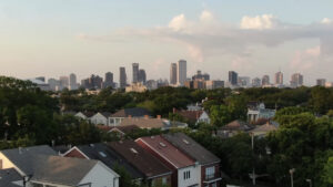 Aerial view of a residential neighborhood with tree-lined streets in the foreground, leading to the skyline of New Orleans