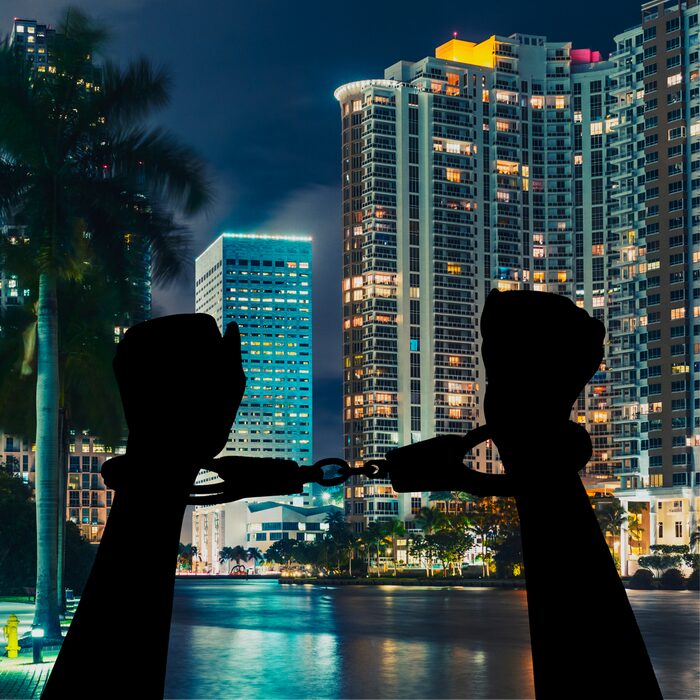 Silhouette of human arms in handcuffs with Miami's tall buildings are in the distance