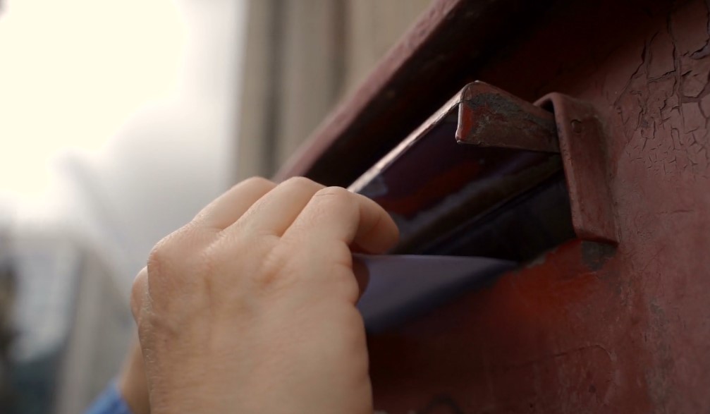 A person is throwing a letter in someone's mail box