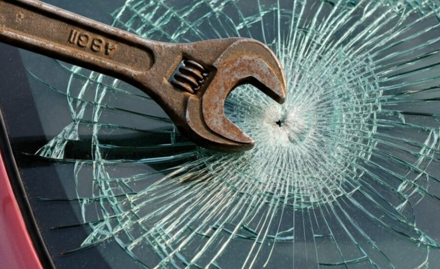 Old rust wrench breaking glass on a car window