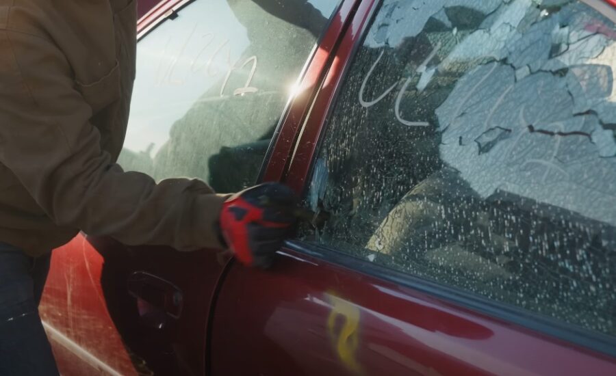 A photo of a human's arm wearing gloves and breaking car's window