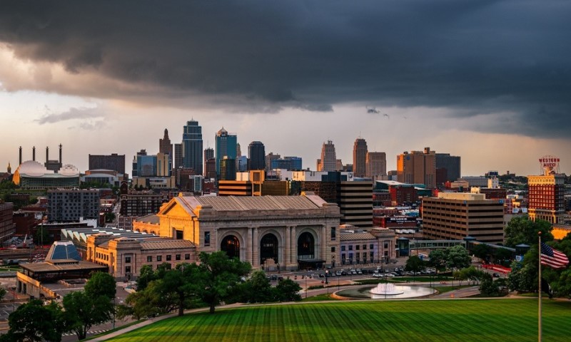 Panoramic view of a Kansas City skyline at sunset. A dark, dramatic storm cloud looms above