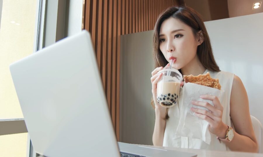 Asian girl drinks white coffee while holding a food and looking at the laptop