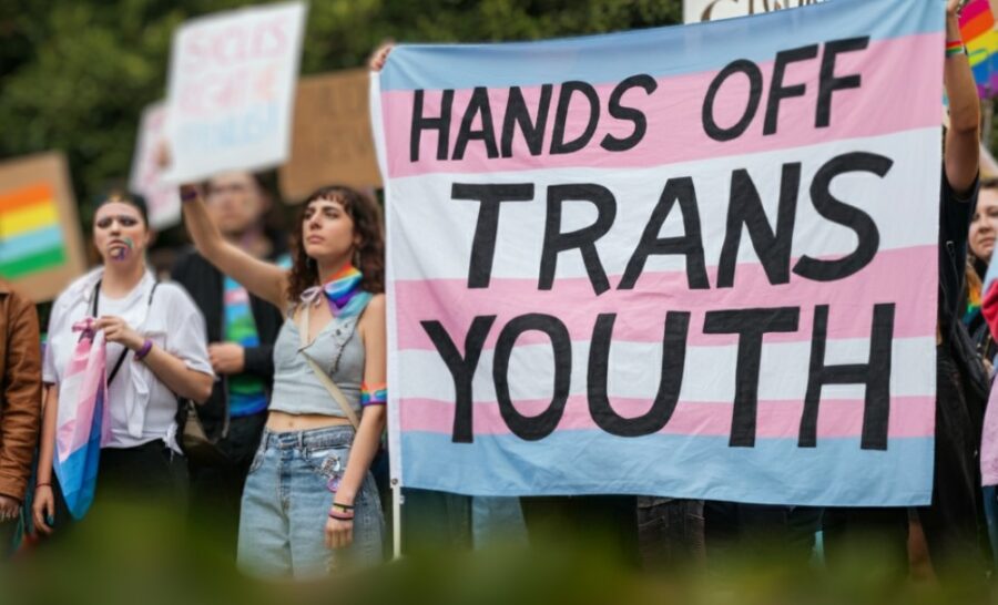 Young LGBT members holding huge banner that says "Hands Off Trans Youth"