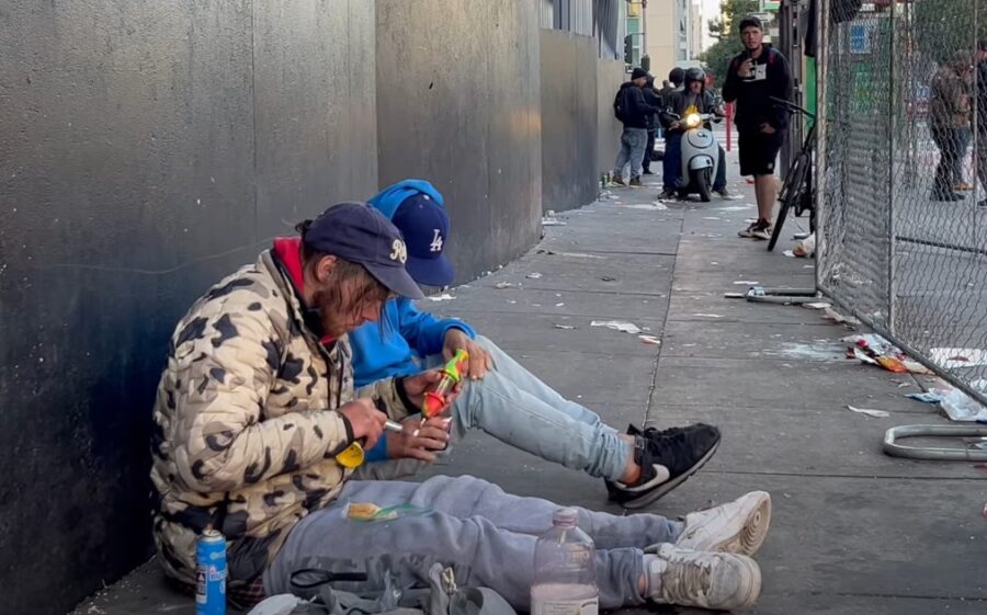 Two homeless persons sitting on the sidewalk