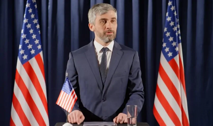 Man gives a speech behind a podium, in front of two American flags