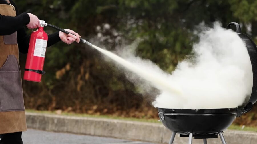 person using a fire extinguisher on a charcoal grill