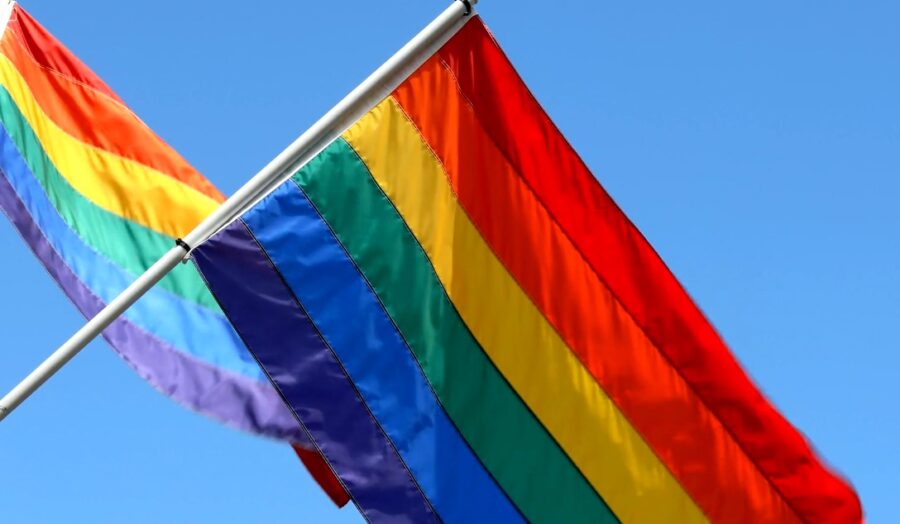 Two LGBT flags on a pole with clear blue sky in the background