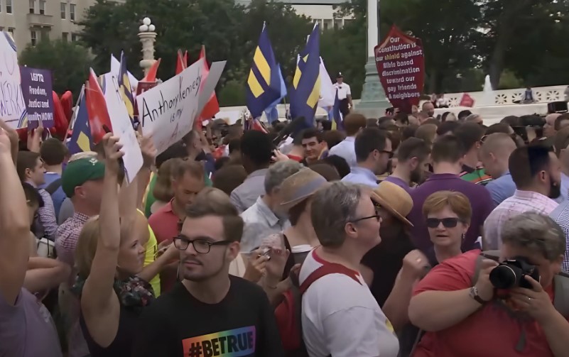 A diverse crowd gathers, holding signs and banners, advocating for equality