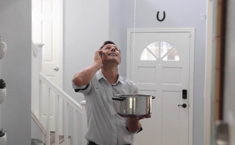 A man, holding a pot to catch dripping water, calls a repair service