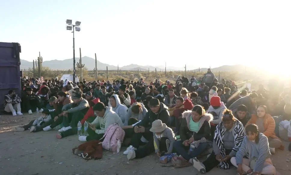 A large group of immigrants sits on the ground