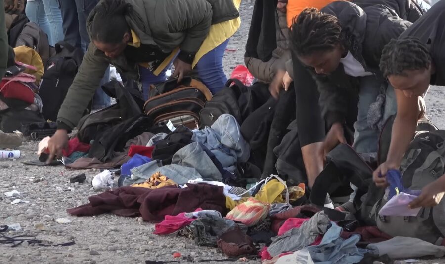 Discarded belongings litter the ground, as immigrants meticulously sort through luggage