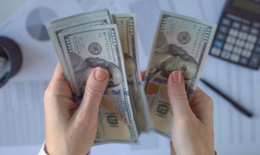 Stacks of US dollars held in hands, surrounded by financial documents