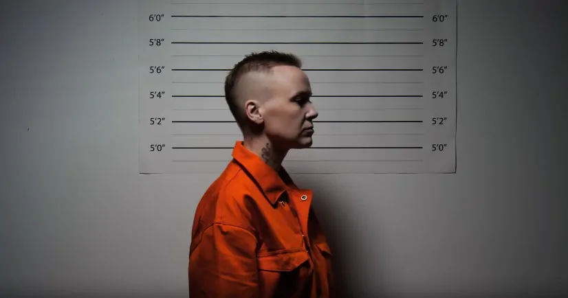 A man in an orange shirt stands before a mug shot backdrop