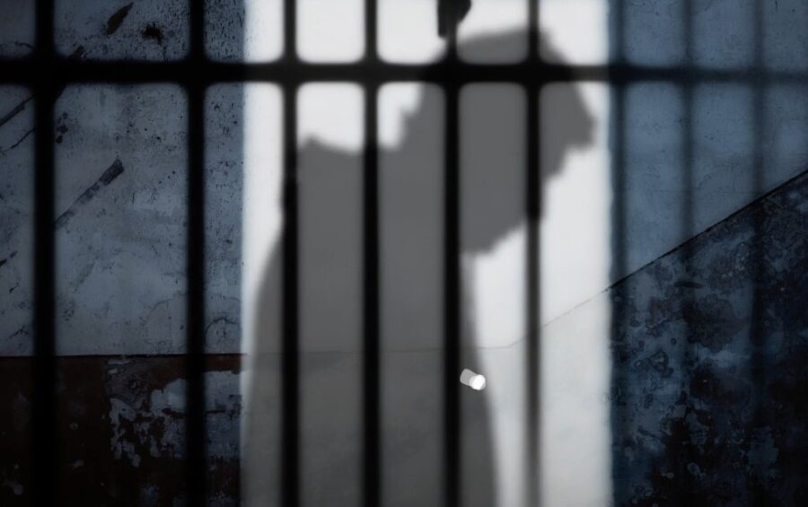 A shadowed figure, confined by jail bars