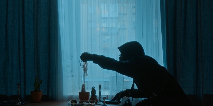 A burglar in silhouette reaches for jewelry near a window