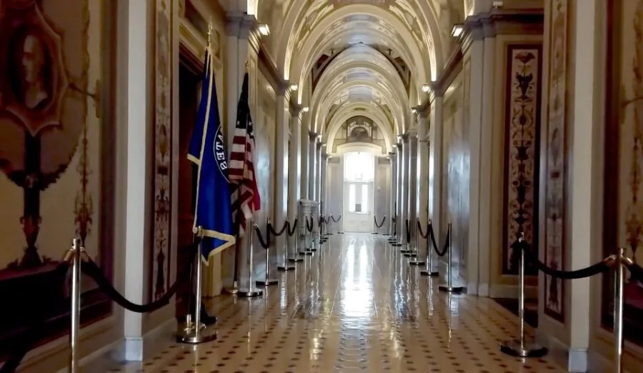 A grand hallway, bathed in light, stretches into the distance, reflecting the grandeur of the building. Flags stand guard, silent sentinels