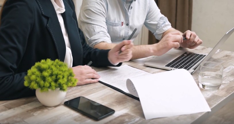 Close-up view of hands working on paperwork and a laptop, suggesting a focused business meeting