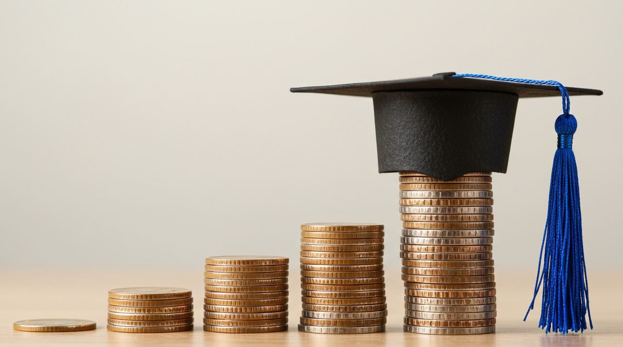 A graduation cap rests atop stacks of coins