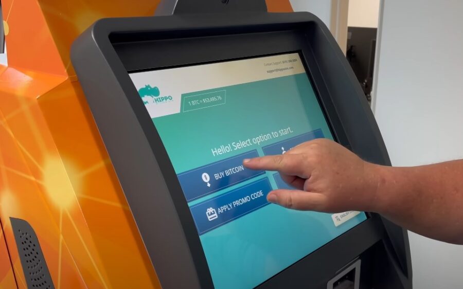 Fingertip hovers over the "Buy Bitcoin" button on a digital kiosk