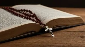 An open book, filled with scripture, rests beside a rosary and crucifix