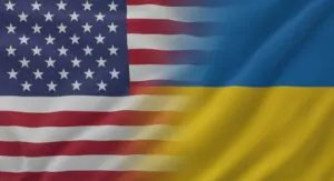 A digitally blended image showing the United States flag on the left and the Ukraine flag on the right, both waving in the wind. The transition between the two flags is smooth and slightly blurred in the center, symbolizing unity and partnership. The fabric texture is visible, and the lighting highlights the folds and motion of the flags