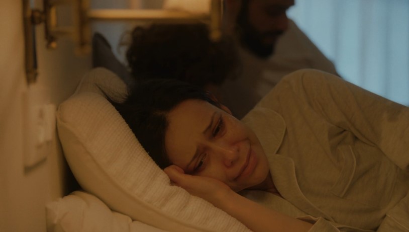 A woman lies in bed, tears streaming down her face, lost in a moment of profound sadness