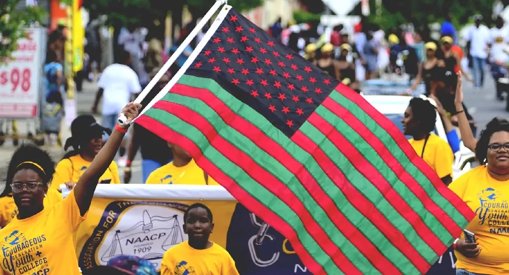 Participants proudly carry a red, black, and green Pan-African American flag during a Juneteenth 2025 parade, honoring freedom and cultural pride