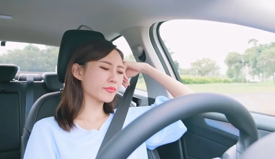 Woman rests her head on her hand, appearing tired behind the wheel.