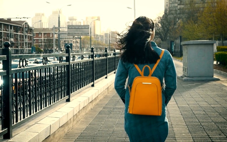 A woman with a vibrant orange backpack, walking