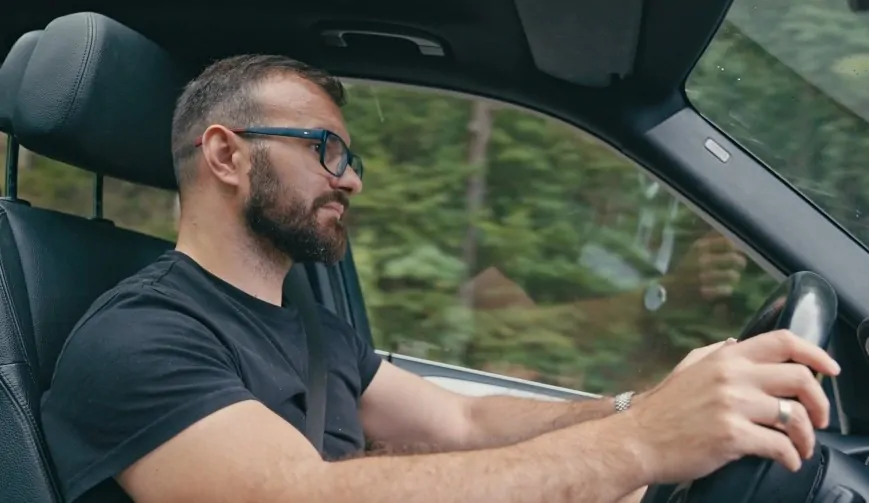 Close-up view of a man driving a car, hands on the steering wheel