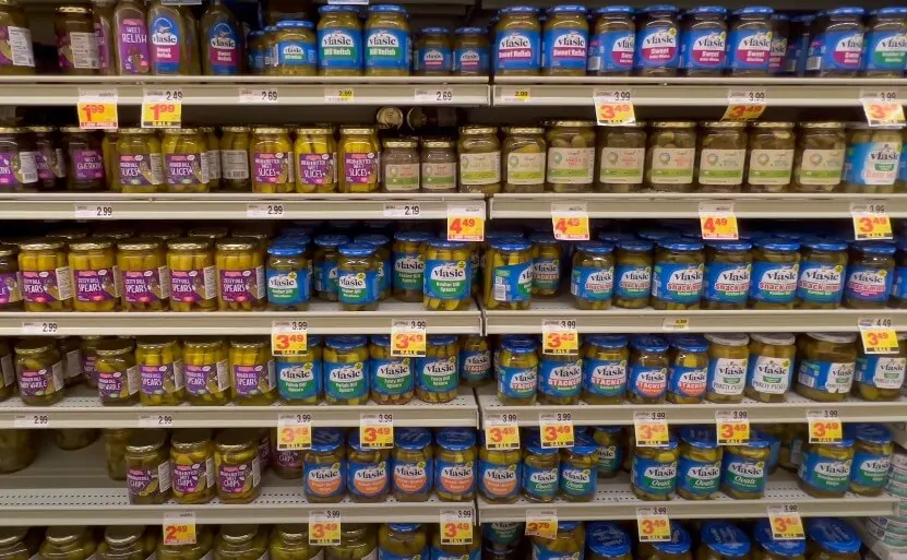 Rows of glass jars, filled with various pickled vegetables, line the supermarket shelves
