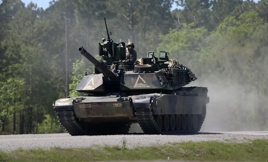 A military tank moves across a gravel road