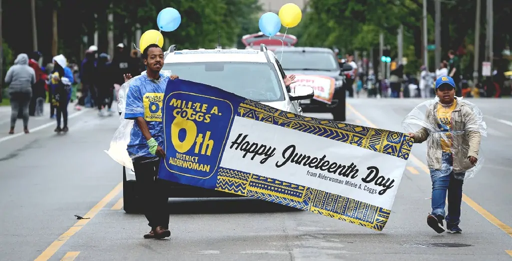 A cheerful Juneteenth 2025 parade procession with community members celebrating freedom and progress with banners and balloons