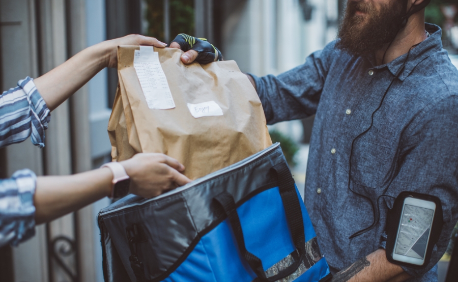 A delivery driver hands off food, showing Boston’s new permit rule for delivery companies