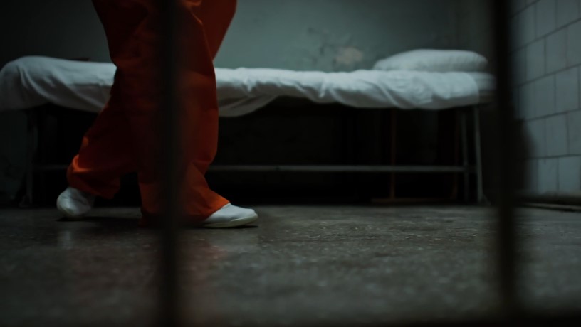 A prisoner's feet, clad in orange, move across the concrete floor of a cell