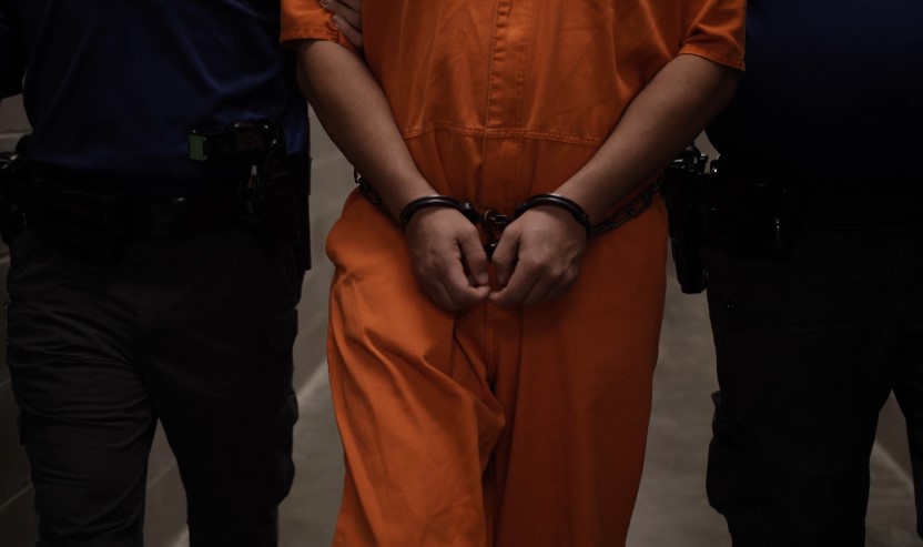 A handcuffed individual in an orange jumpsuit