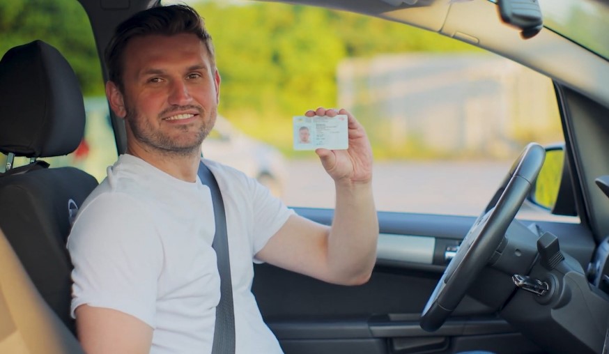 Man driver holding driver licence while sitting in a car