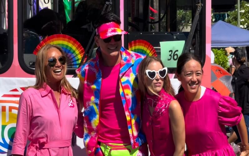 A group of people in pink outfits stands beside a bus, smiling and posing for the camera