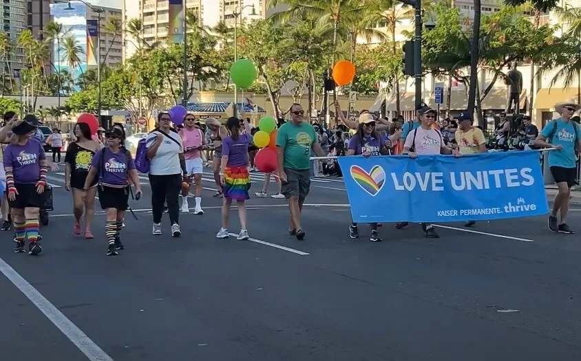 A diverse group of people walking together, holding a banner that reads "Love United" in a vibrant street setting