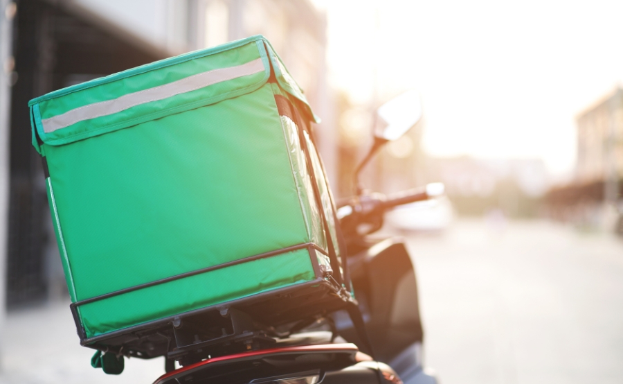 A green delivery bag sits on a parked scooter, hinting at drivers’ reactions to Boston’s new delivery rules