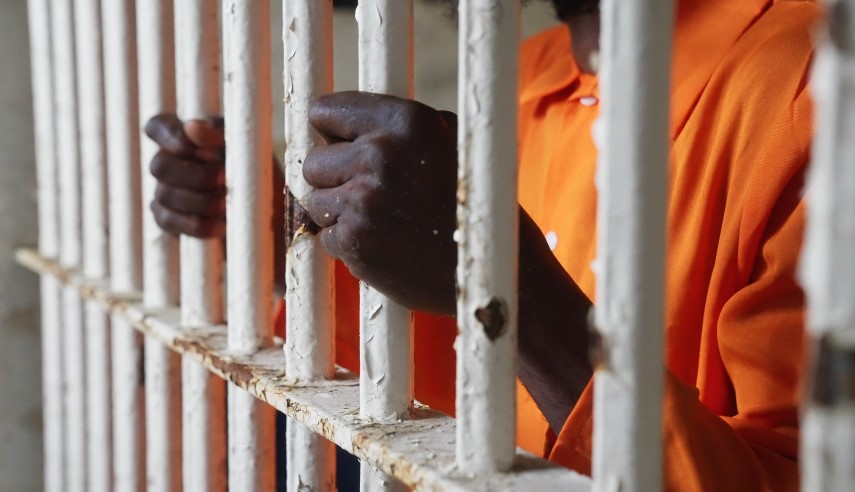 Hands clasped tightly around prison bars, a prisoner's gaze directed inward